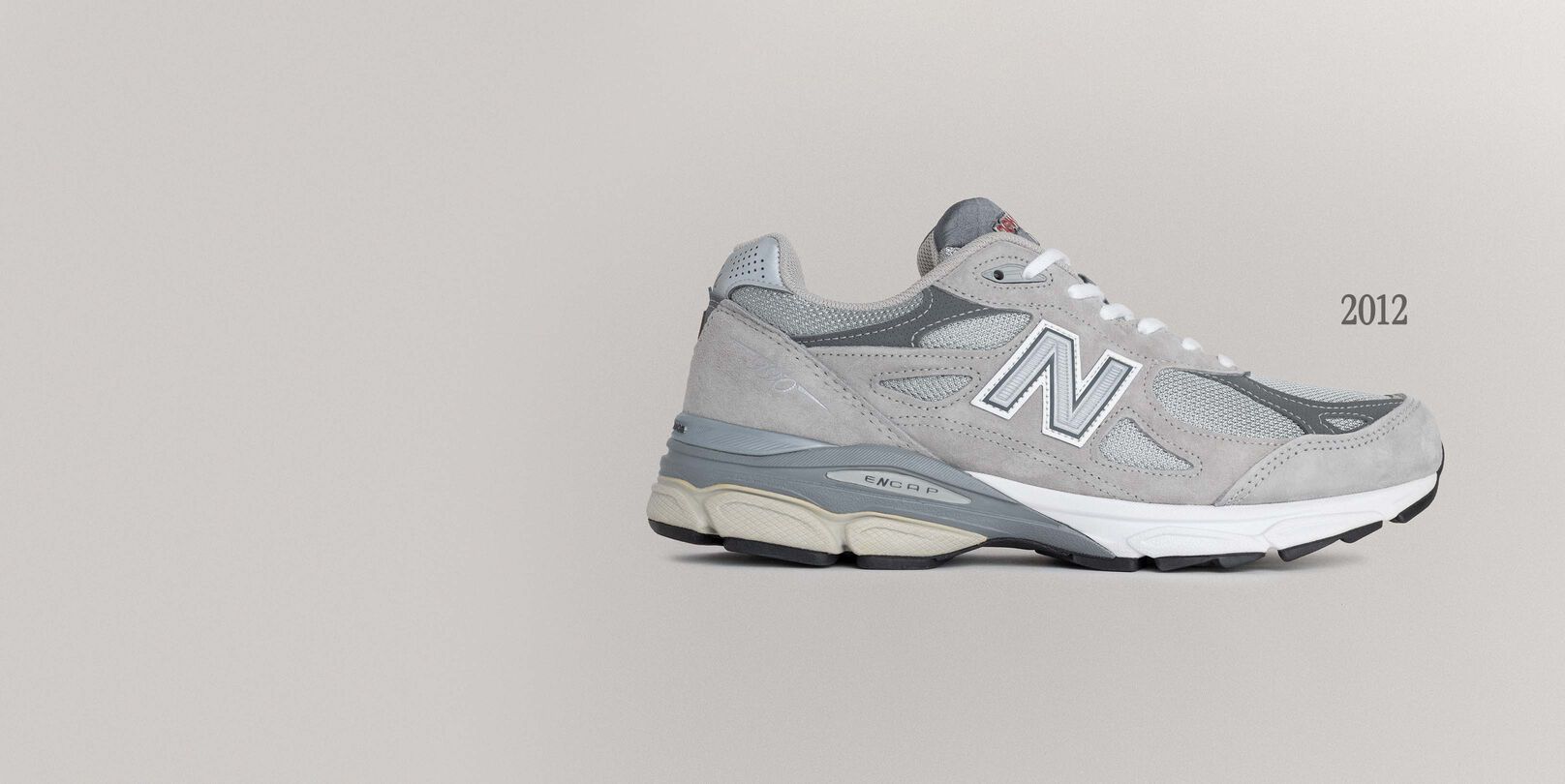 A grey 990v3 sneaker sitting on a grey background.