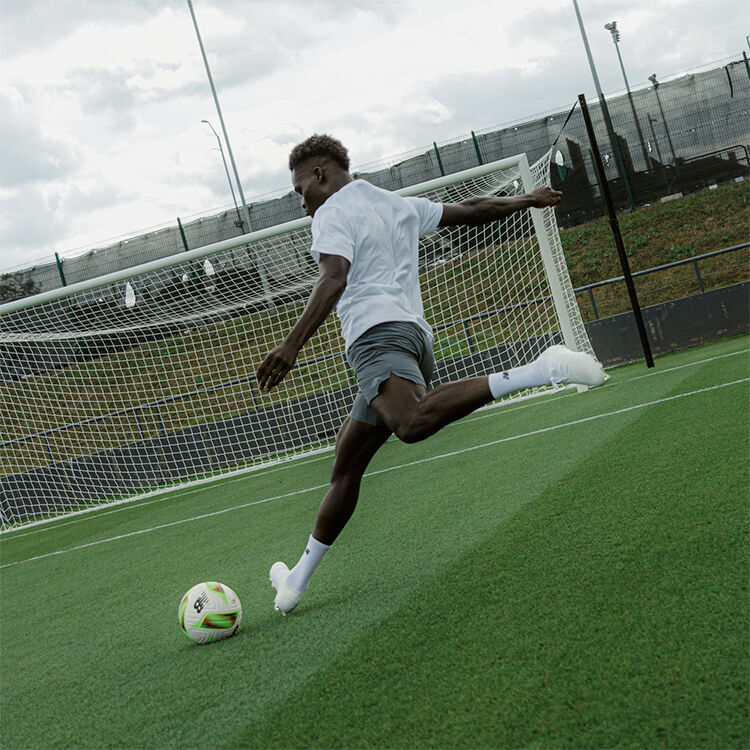 bukayo saka kicking a football ball to an emty goal with new balance football boots