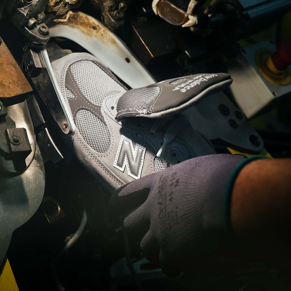 A hand putting a sneaker into a machine during its construction.  