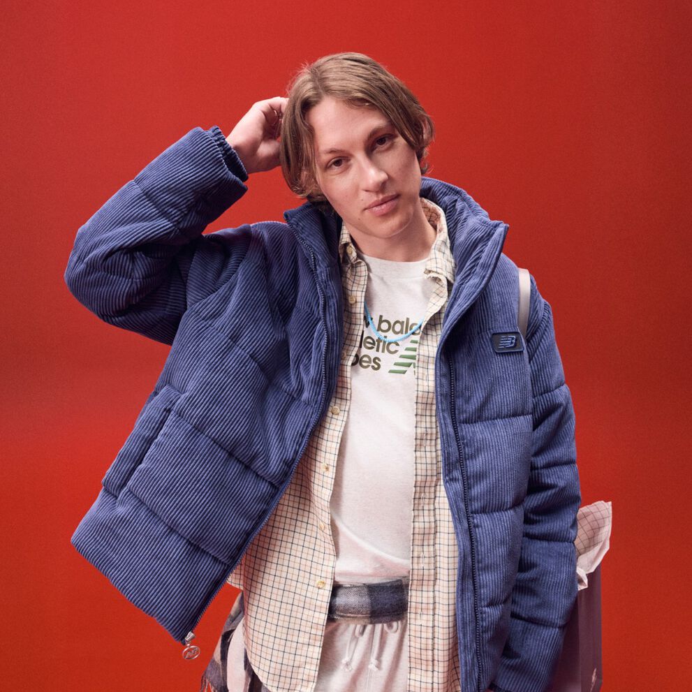Young man in a blue coat scratching his head on a red background.