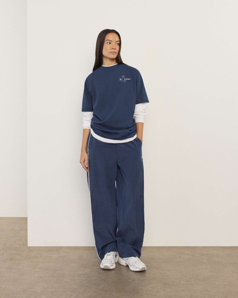 A woman wearing New Balance standing in front a white wall.